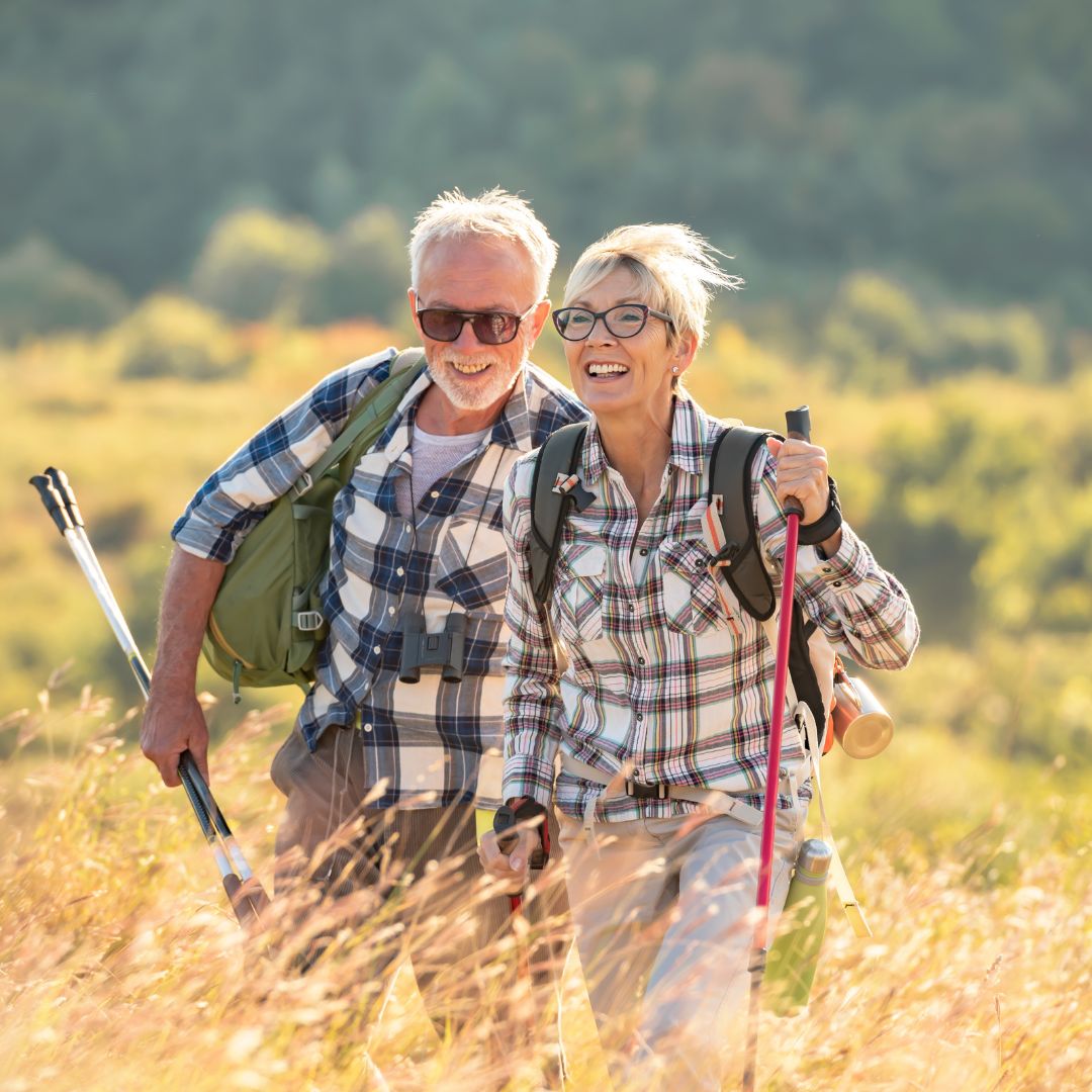 Älteres Paar wandert mit Wanderstöcken auf einem Feld.