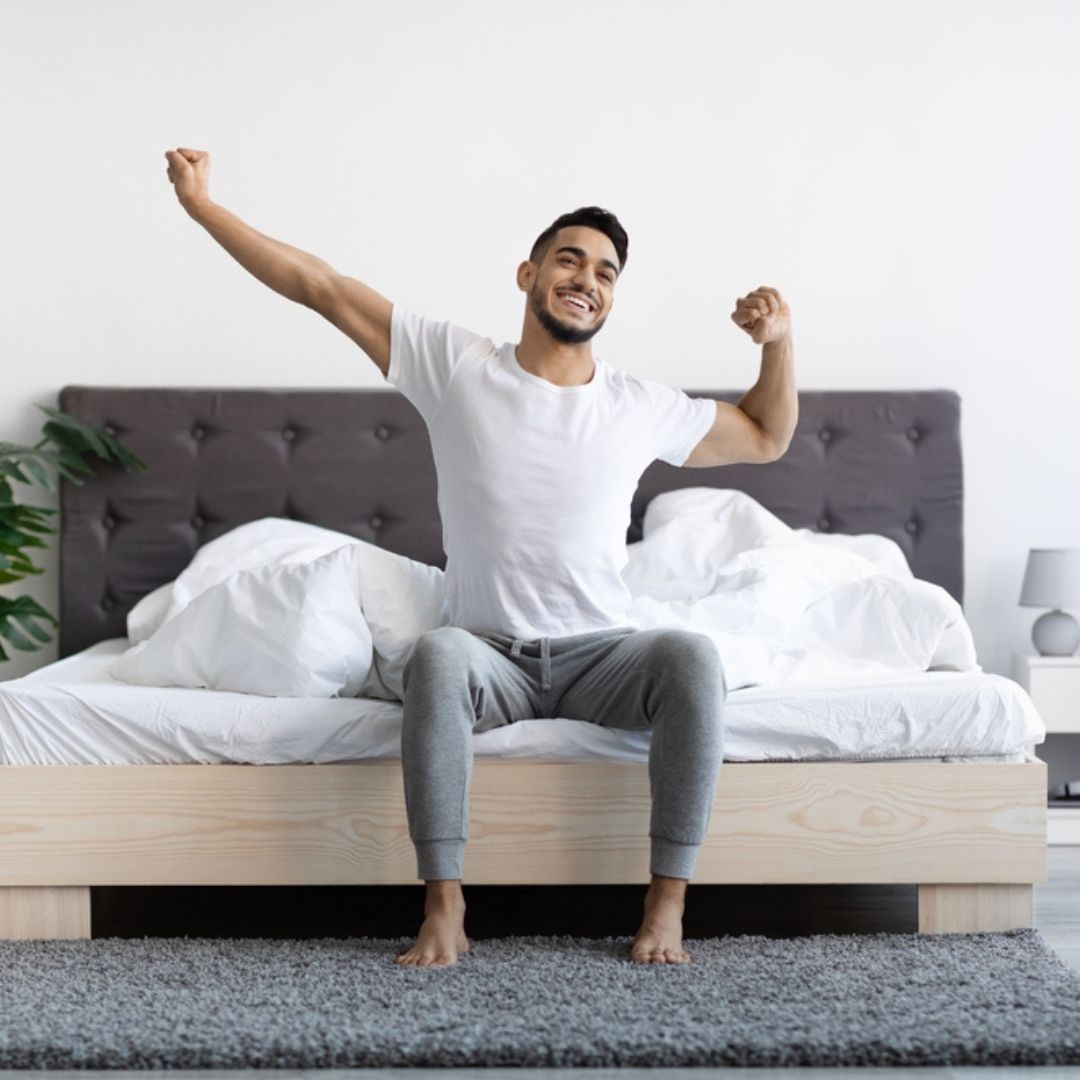 Ein Mann sitzt auf einem Bett und streckt die Arme in die Luft.